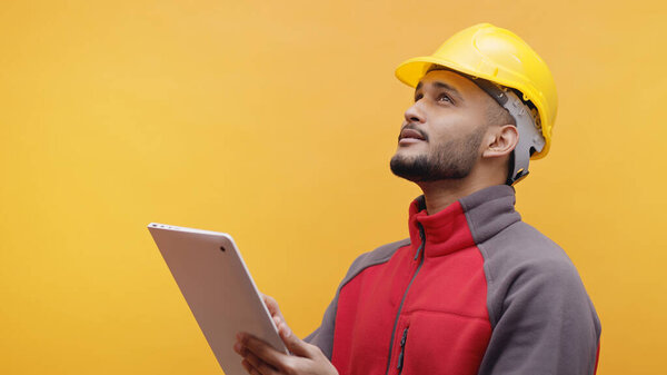 A Young Engineer Wearing Yellow Safety Helmet Holding A Tablet In His Hand 