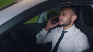 Genç Çalışan, arabanın sürücü koltuğunda oturmuş telefonda biriyle konuşuyor.