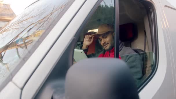 Tipo de entrega con gorra sentada en el asiento delantero de la camioneta blanca usando tableta — Vídeo de stock