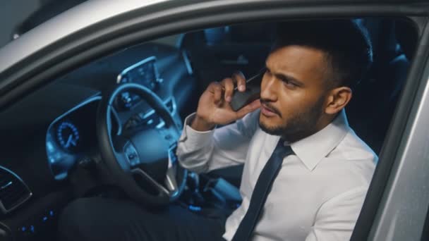 Wściekły młody biznesmen rozmawia z kimś przez telefon siedząc w samochodzie — Wideo stockowe