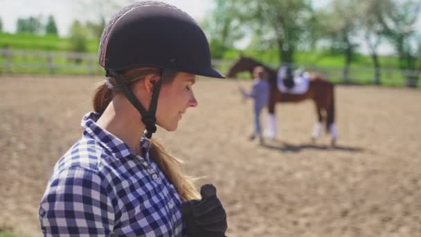 Reiterin mit Helm lächelt in die Kamera Pferd im Hintergrund — Stockvideo