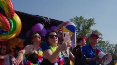 Renkli bayrakları ve hoparlörleri olan insanlar dans edip fotoğraf çekiyorlar. LGBTQ hakları için yürüyüş yapıyorlar.