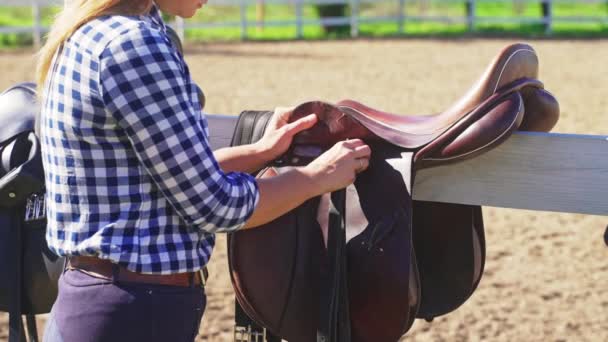 Mladá dívka visí kožené sedla na dřevěném plotě během dne — Stock video