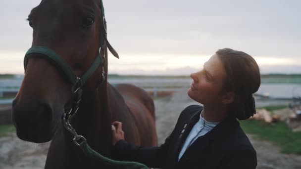 Paardeneigenaar draagt een zwarte jas glimlachend naar haar zegel bruin paard in de ranch — Stockvideo