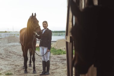 Karanlık sahil atıyla dışarıda duran bir kadın kameraya ahır pozu veriyor