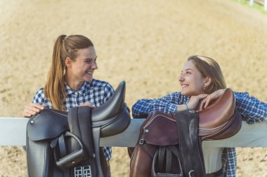 Elleri tahta çitin üzerinde duran kızlar Çitin üzerinde asılı duran eyerler