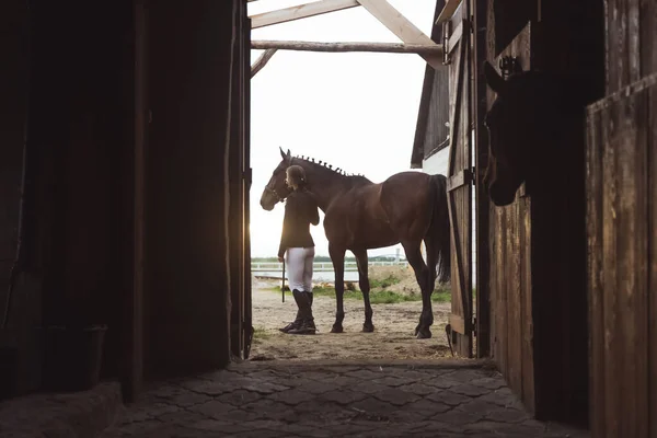 Mulher de cavalo com seu cavalo de baía escuro no rancho de cavalos - Vista do estábulo — Fotografia de Stock
