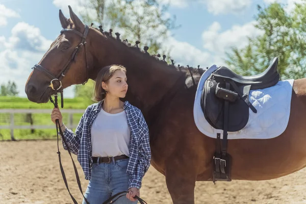 Menina nova com seu cavalo escuro da baía que está na corda principal estável do cavalo da preensão — Fotografia de Stock