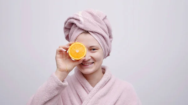 Vrolijk meisje met hoofddoek en een badjas met oranje plakje in haar hand — Stockfoto