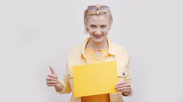 Mädchen hält ein gelbes Blatt Papier lächelnd in der Hand und macht ein Daumenhoch-Zeichen — Stockfoto