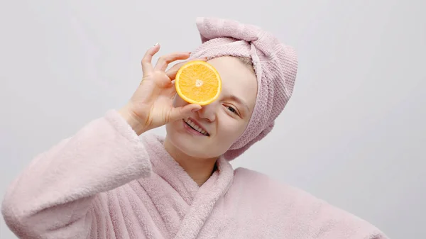 Meisje houdt half oranje en bedekt haar oog met de sinaasappel - hydraterende huid — Stockfoto