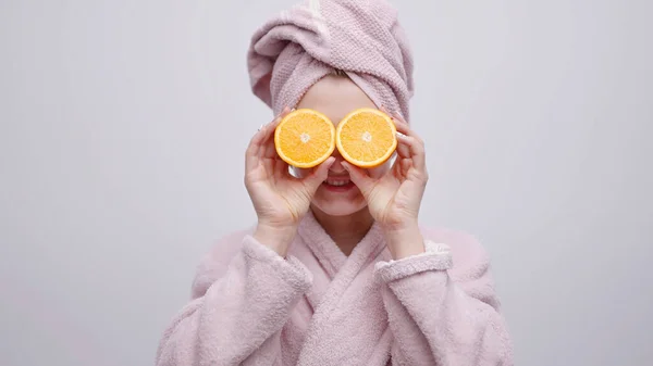 Meisje dragen hoofd handdoek en een badjas houden twee oranje plakken in haar hand — Stockfoto