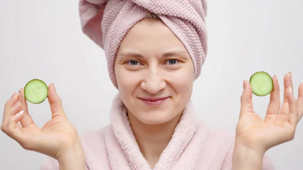 Meisje met een hoofd handdoek dragen een roze badjas Holding komkommer plakken - huidverzorging — Stockfoto