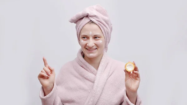 Meisje houden een kleine pot van hydraterende huid crème aanbrengen crème op haar gezicht — Stockfoto