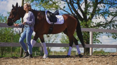 Genç bir kadın kahverengi bir atın üzerinde hafifçe yürür.