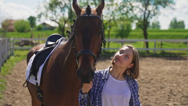 A young beautiful brunette looks at the horse next to her on the ranch — Stock Photo, Image