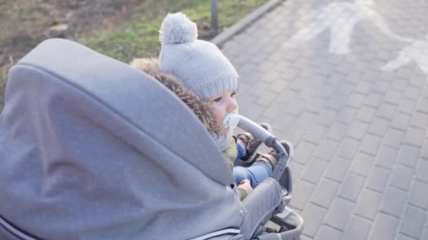 Толкая очень маленького ребенка красиво одетого с пустышкой во рту на бетонной дорожке — стоковое видео