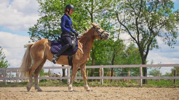 Uma jóquei fêmea de comprimento total senta-se em um cavalo marrom claro em um rancho — Fotografia de Stock