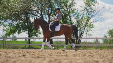 Genç bir kız, dört nala koşan kahverengi bir atın üzerinde dik oturur.