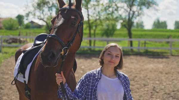 A young girl in an unbuttoned shirt and white T-shirt holds a horse by the reins — Stock Photo, Image