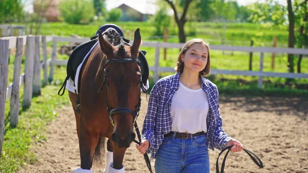 A young girl in an unbuttoned shirt, white T-shirt with a smile on her face, holding the horse behind her — Stock Photo, Image