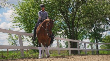 Genç bir kız kahverengi bir atın üzerinde oturmuş yere bakıyor.