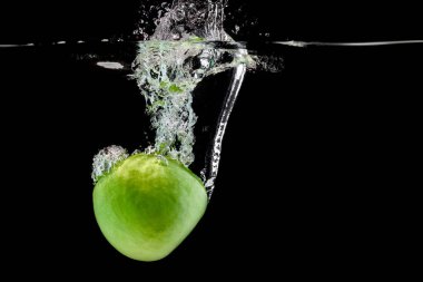 Suya düşen yeşil elma ve siyah bir arka plan.