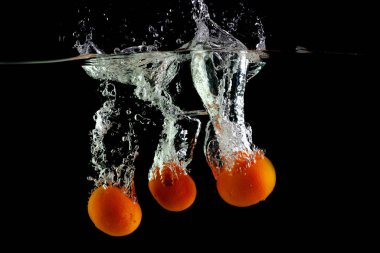 Üç mandalina siyah bir zeminde suya düşer.