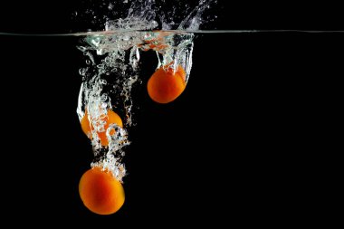 Üç mandalina siyah bir zeminde suya düşer.