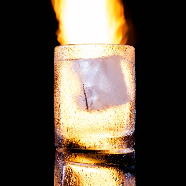Glass with a piece of ice against the background of fire — Stock Photo, Image