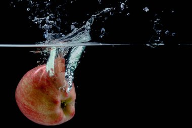 Kırmızı elma suya düşer, siyah arkaplan üzerinde sıçramalar, metin altında konum