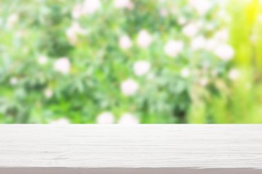 Bulanık çalıların üzerindeki beyaz ahşap masa.