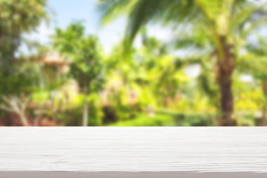 Bulanık tropik bitki arka planında beyaz ahşap masa