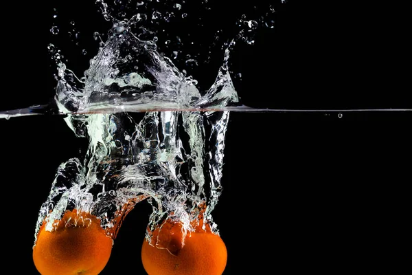 two tangerines fall into the water on a black background, copy space