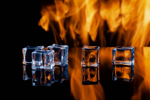 Cinco cubitos de hielo sobre un fondo negro, en el fondo llamas —  Fotos de Stock