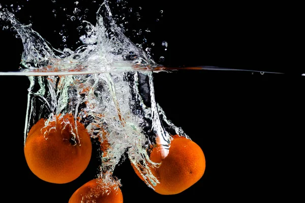 Tre mandarini cadono in acqua su uno sfondo nero, copiare lo spazio — Foto Stock