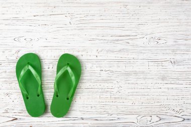Beyaz ahşap zemin üzerinde yeşil lastik terlikler, yukarıdan görüş, metnin altında yer
