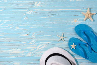 Mavi ahşap arka planda şapka ve plaj terlikleri. Denizyıldızı. Yukarıdan görüntüle