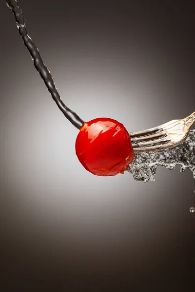 小樱桃西红柿在银叉子上倒入水。飞溅的水。优雅的背景。垂直框架。放在案文中 — 图库照片