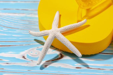 Sarı kauçuk plaj terlikleri ve mavi ahşap arka planda deniz yıldızı, metnin altına.
