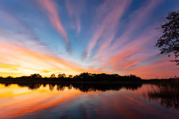 Nehrin üzerinde gün batımı, ormanın silueti, suda ayna görüntüsü.