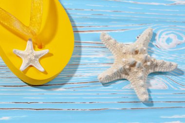 Sarı kauçuk plaj terlikleri ve mavi ahşap arka planda deniz yıldızı, metnin altına.