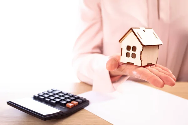 Vrouw houdt model van huis bij de hand, op de tafel ligt een contract en rekenmachine Stockfoto