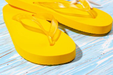 Sarı kauçuk plaj terlikleri ve mavi ahşap arka planda deniz yıldızı, metnin altına.