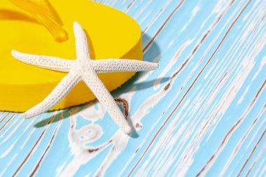 Sarı kauçuk plaj terlikleri ve mavi ahşap arka planda deniz yıldızı, metnin altına.