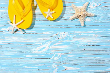 Sarı kauçuk plaj terlikleri ve mavi ahşap arka planda deniz yıldızı, metnin altına.
