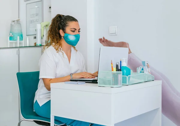 female physiotherapist with face mask working in clinic, talking with patient in video chat, writing and checking radiographics of patient.