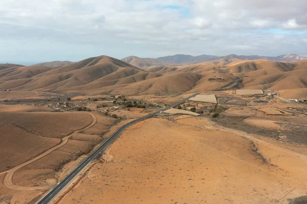 Beautiful drone footage of a winding highway traversing the mountainous region of Sicasumbre in Fuerteventura, Canary Islands. The video showcases the contrast between the smooth asphalt curves and the harsh, rocky desert scenery of the islands 