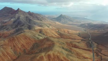 Sicasumbre dağlarının ve Fuerteventura 'daki dolambaçlı yolun hava aracı görüntüsü, açık mavi gökyüzünün altındaki volkanik manzaraları ve çöl tepelerini gösteriyor..