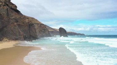 Fuerteventura, Kanarya Adaları 'ndaki Coffee Beach' in sersemletici hava görüntülerinde karamsar, bulutlu bir gökyüzü altında ikonik Roque del Moro kaya oluşumu görülüyor. Uzak ve dramatik bir Atlantik manzarası.